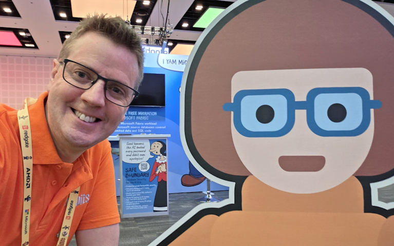 A smiling man wearing glasses and an orange SQLBits polo shirt poses beside a large cartoon character with blue glasses at a technology conference. Exhibition stands and promotional displays are visible in the background.
